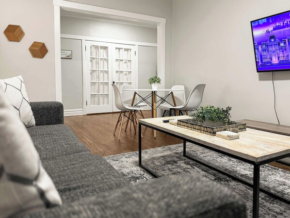 Una sala de estar moderna con un sofá gris, una mesa de centro y un televisor montado en la pared.