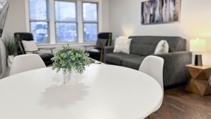 A modern living room with a round white table, grey sofa, and a potted plant.