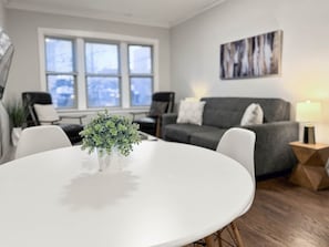 Una sala moderna con una mesa redonda blanca, un sofá gris y una planta en maceta.