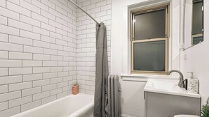 A bathroom with a white bathtub, a window above the sink, and a radiator.