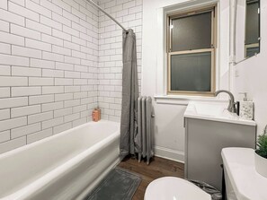 Un baño con una bañera blanca, una ventana sobre el lavamanos y un radiador.