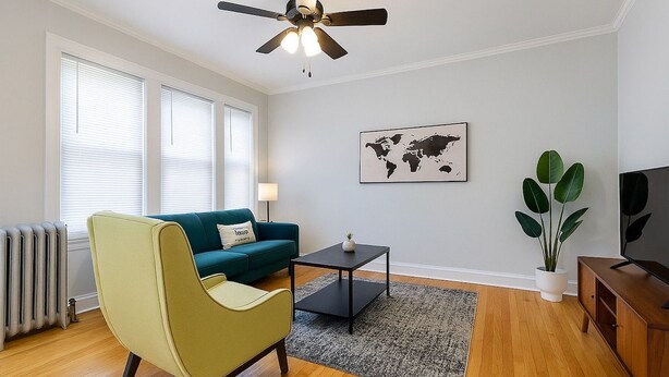 A living room with a teal sofa, a green armchair, a coffee table, a world map on the wall, a plant, and a TV on a wooden cabinet. - Cozy 1BR in Walkable Area (Chicago)