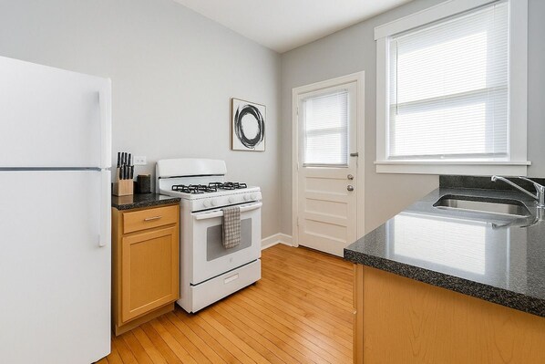 A kitchen with a white refrigerator, a stove, a sink, wooden cabinets, and a window with blinds.