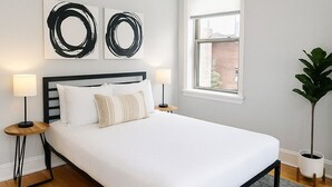 A bedroom with a bed, a ceiling fan, two wall art pieces, a window, and a potted plant. - Cozy 1BR in Walkable Area (Chicago)