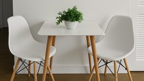 Una habitación moderna con una mesa blanca, dos sillas blancas, una planta en maceta, un cuadro abstracto en blanco y negro, un termostato y una puerta.