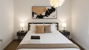 Habitación de hotel ordenada, con una cama grande, dos mesitas de noche y un cuadro abstracto moderno sobre la cama.