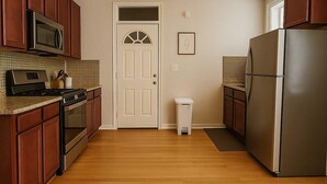 A kitchen with wooden cabinets, stainless steel appliances, a microwave, stove, refrigerator, and a trash can. - Charming 1BR in Old Irving (Chicago)