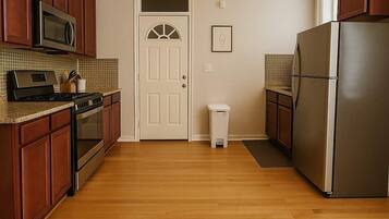 A kitchen with wooden cabinets, stainless steel appliances, a microwave, stove, refrigerator, and a trash can.