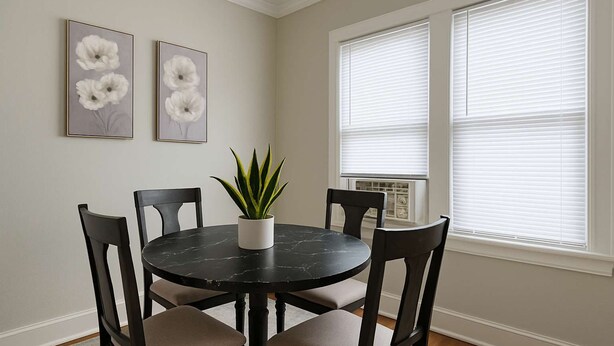 A dining area with a round table, four chairs, a potted plant, and two framed floral artworks on the wall.
