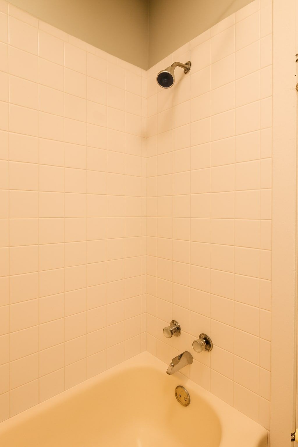 A bathroom with white tiled walls, a bathtub, and a showerhead.