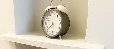 A white shelf with a wall-mounted alarm clock and a potted plant.