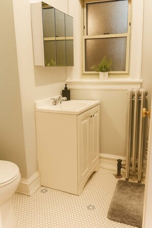 A compact bathroom with a white sink, a toilet, and a window above the sink.