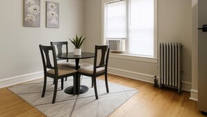 A dining area with a round table, four chairs, a potted plant, and two wall-mounted flower paintings.