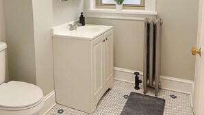 A small bathroom with a toilet, a sink, a mirror, and a window.