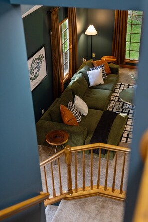 A room with a green sofa, a lamp, and a view of the outdoors through a window. - Heated Pool | Sauna | Hot Tub | Theater | Games (Kalkaska)