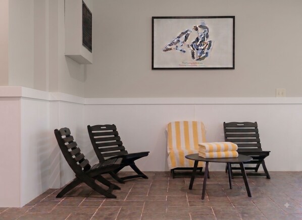 Een kamer met twee zwarte stoelen, een stoel met gele strepen, en een klein rond tafeltje met een opgevouwen handdoek.
