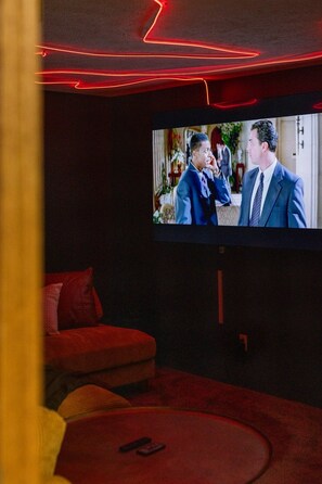Een kamer met een flatscreen televisie aan de muur, een rode bank en een rood tapijt.