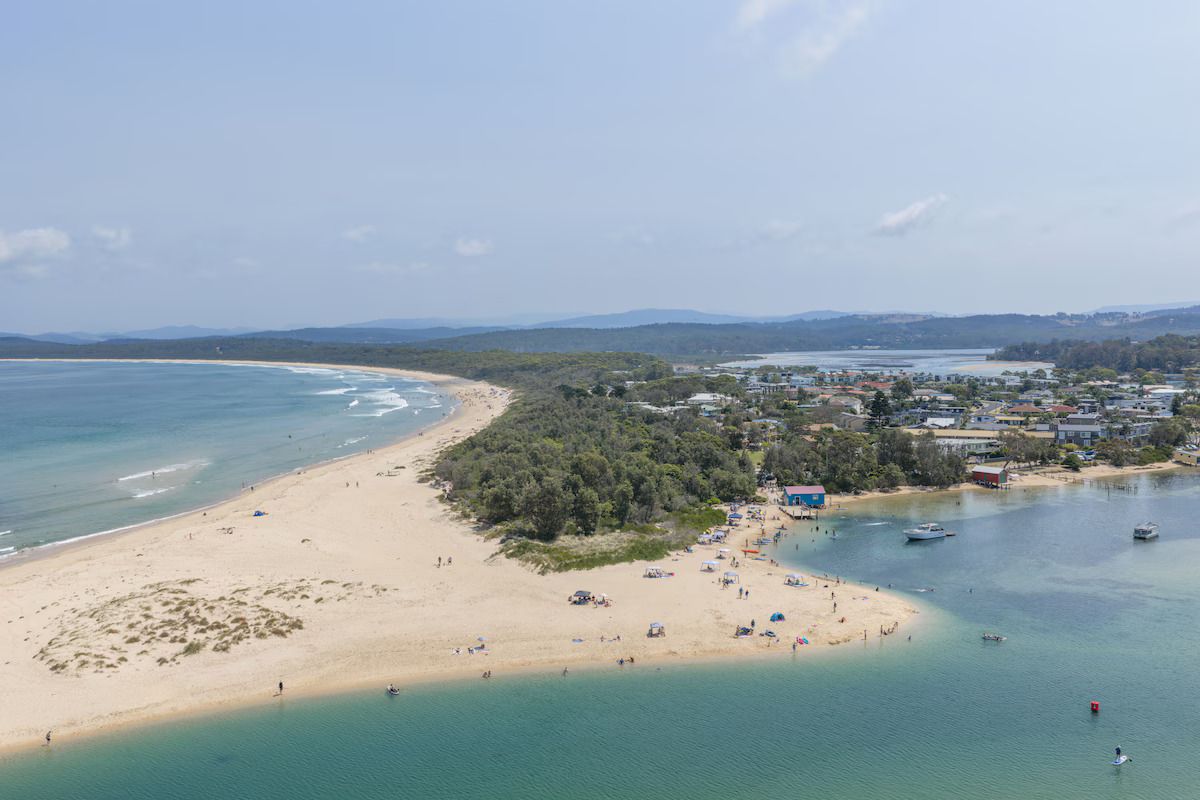 Luchtbeeld van een kustgebied met een strand, boten en een stad op de achtergrond.