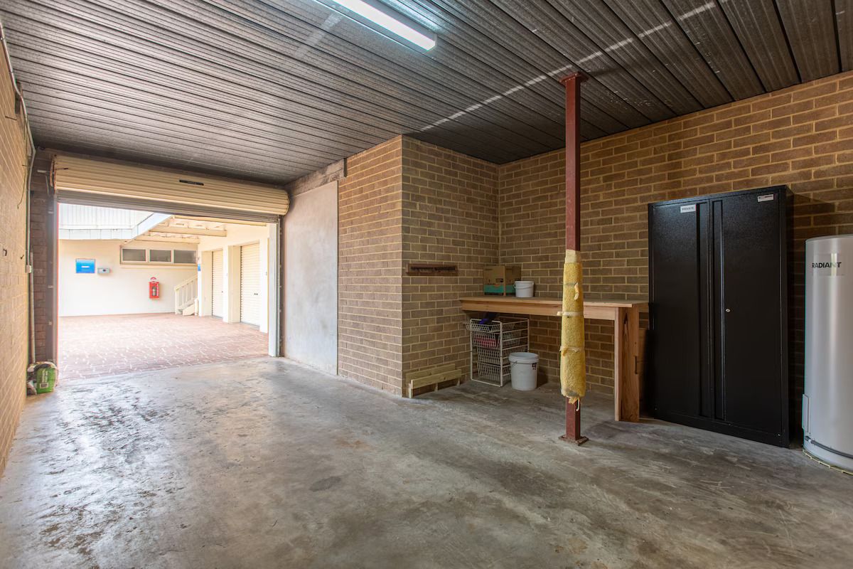 An indoor space with a brick wall, a black refrigerator, a wooden table, and a concrete floor.