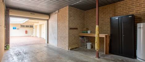 An indoor space with a brick wall, a black refrigerator, a wooden table, and a concrete floor.