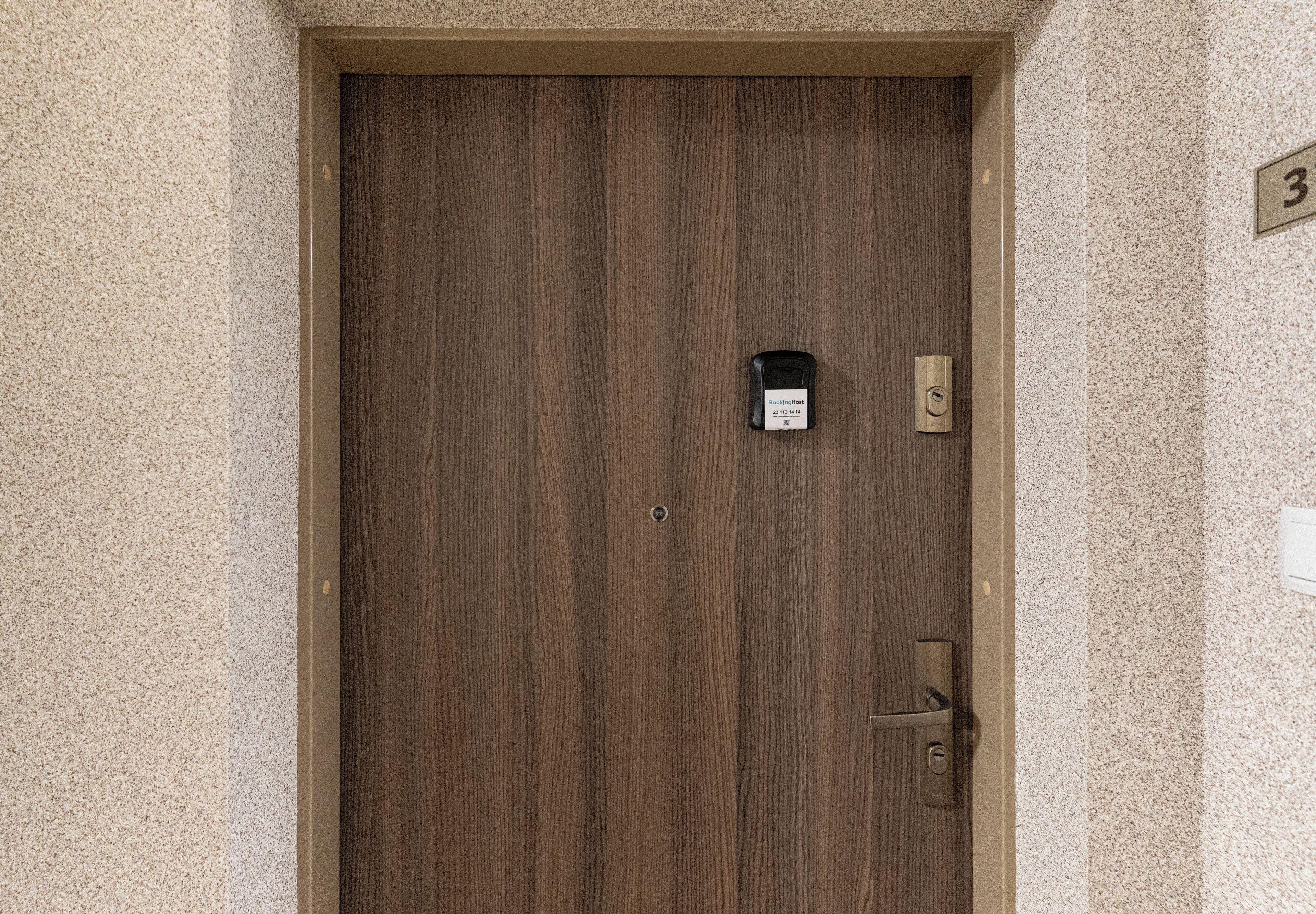 Una puerta de madera con una cerradura y un agujero para la llave, un pequeño dispositivo negro en la puerta, y el número '3' en la pared.