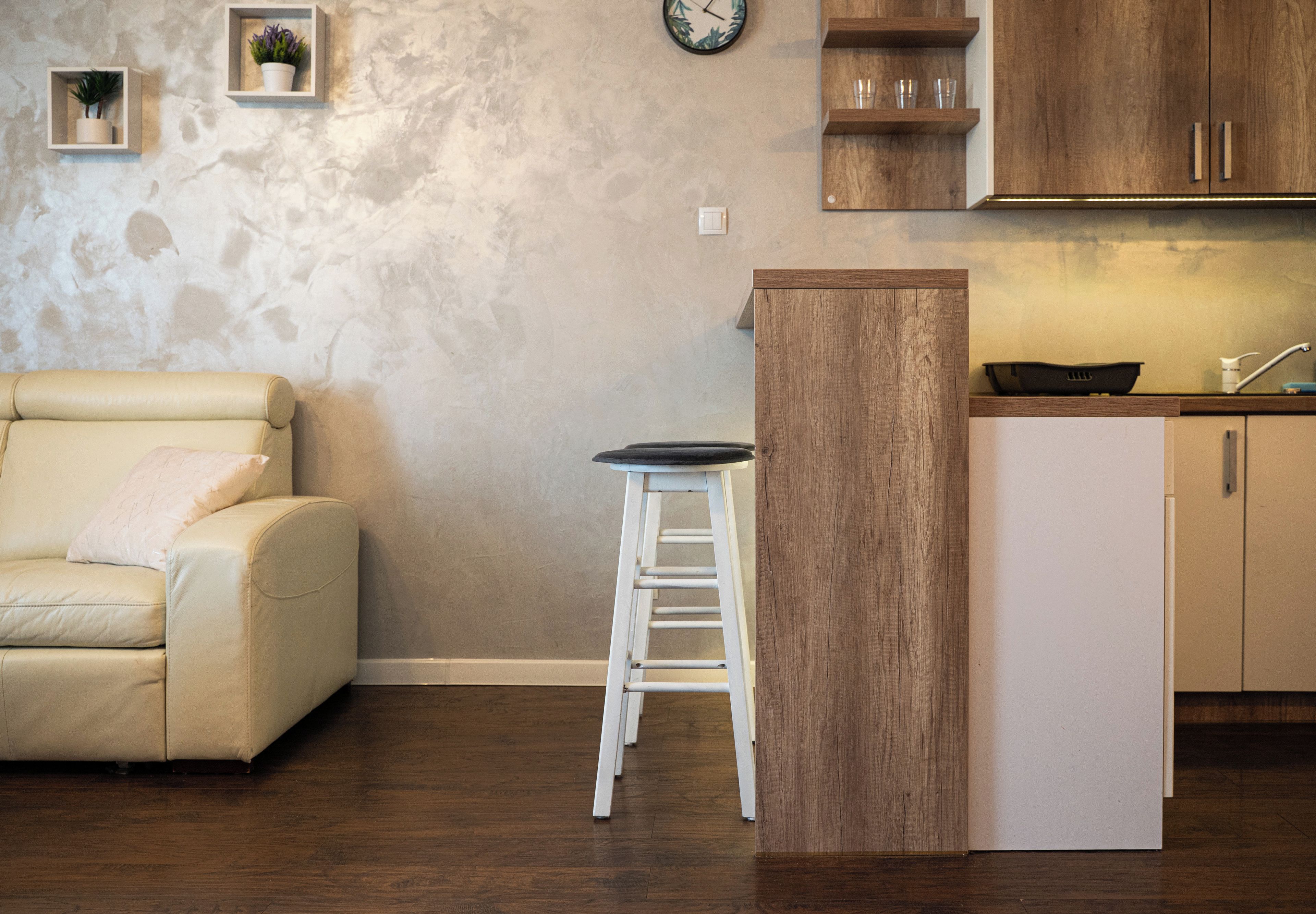 Una cocina moderna con una isla de madera, un taburete blanco y un sofá beige en una sala de estar.