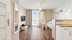 Una sala de estar moderna con un televisor de pantalla plana, un sofá, una mesa de comedor y una zona de cocina con armarios.