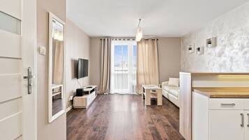 A modern living room with a flat-screen TV, a sofa, a dining table, and a kitchen area with cabinets.
