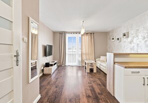 Een moderne woonkamer met een flatscreen televisie, een bank, een eettafel en een keuken met kasten.