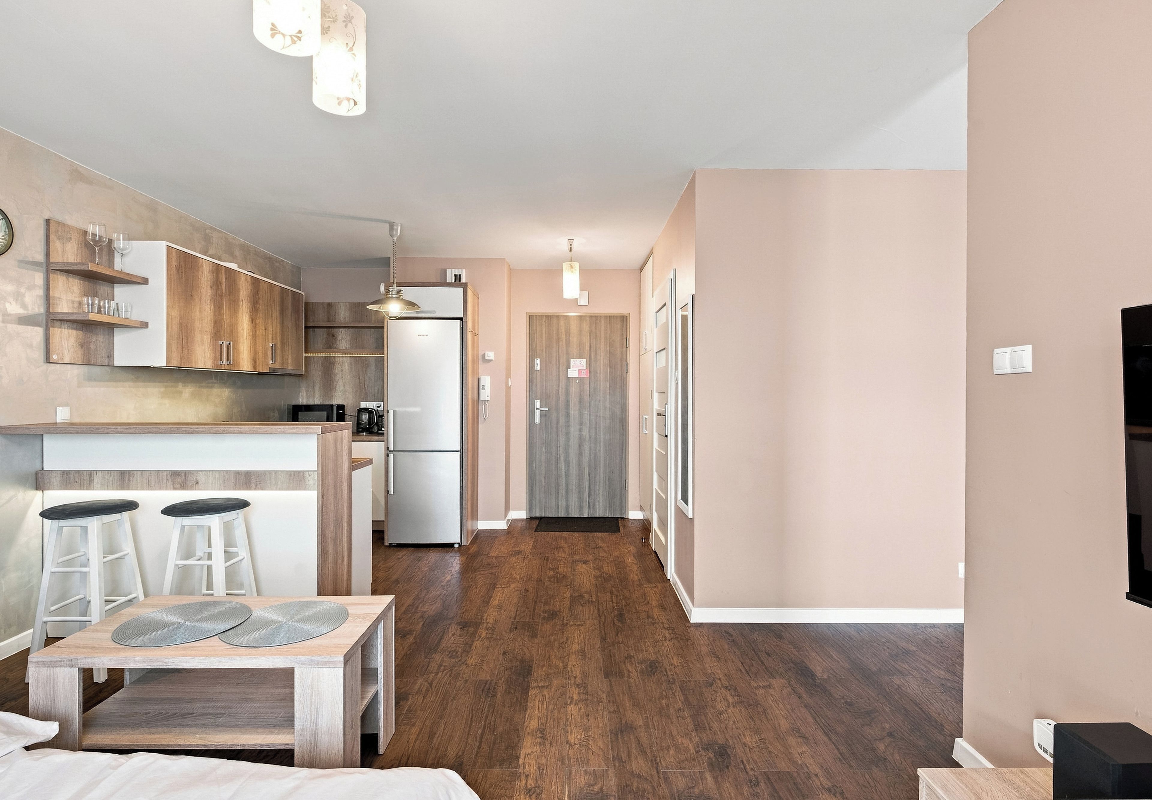 A modern kitchen with wooden cabinets, a refrigerator, and a dining area with stools.