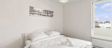 A bedroom with a bed, a hanging light fixture, a window with a view, and a wall-mounted picture.