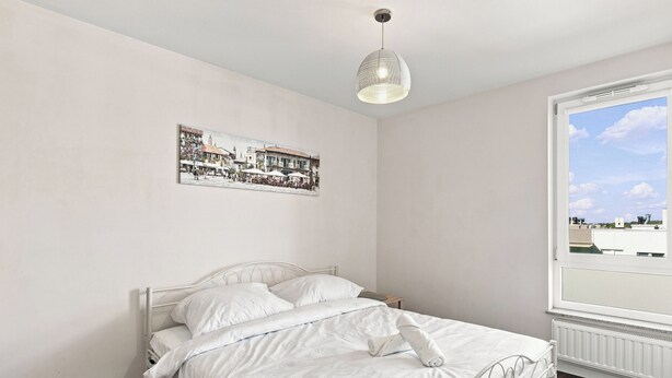 Un dormitorio con cama, lámpara colgante, ventana con vistas y un cuadro en la pared.