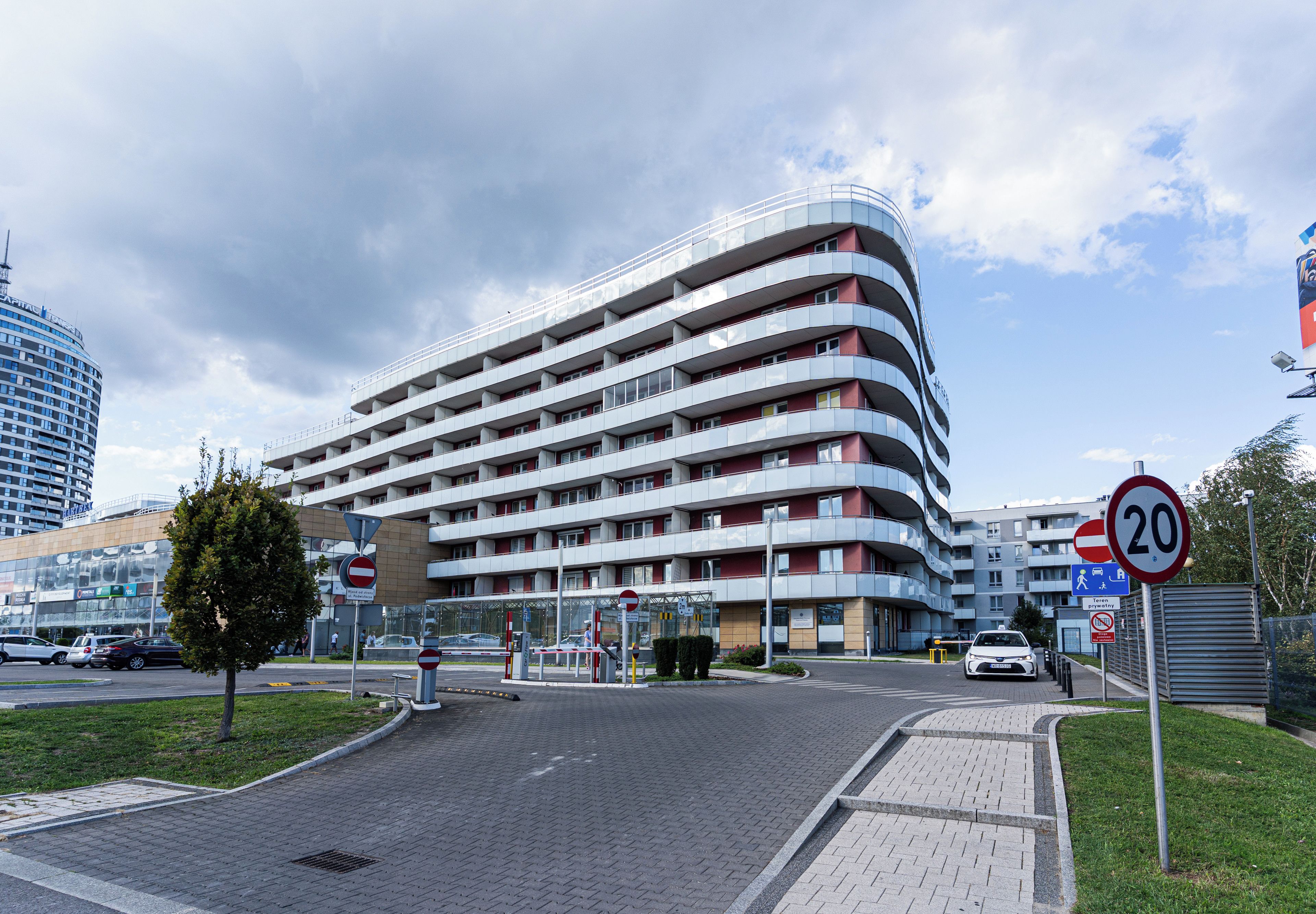 Un hotel de varios pisos con fachada curva, un paso de peatones y una señal de límite de velocidad.
