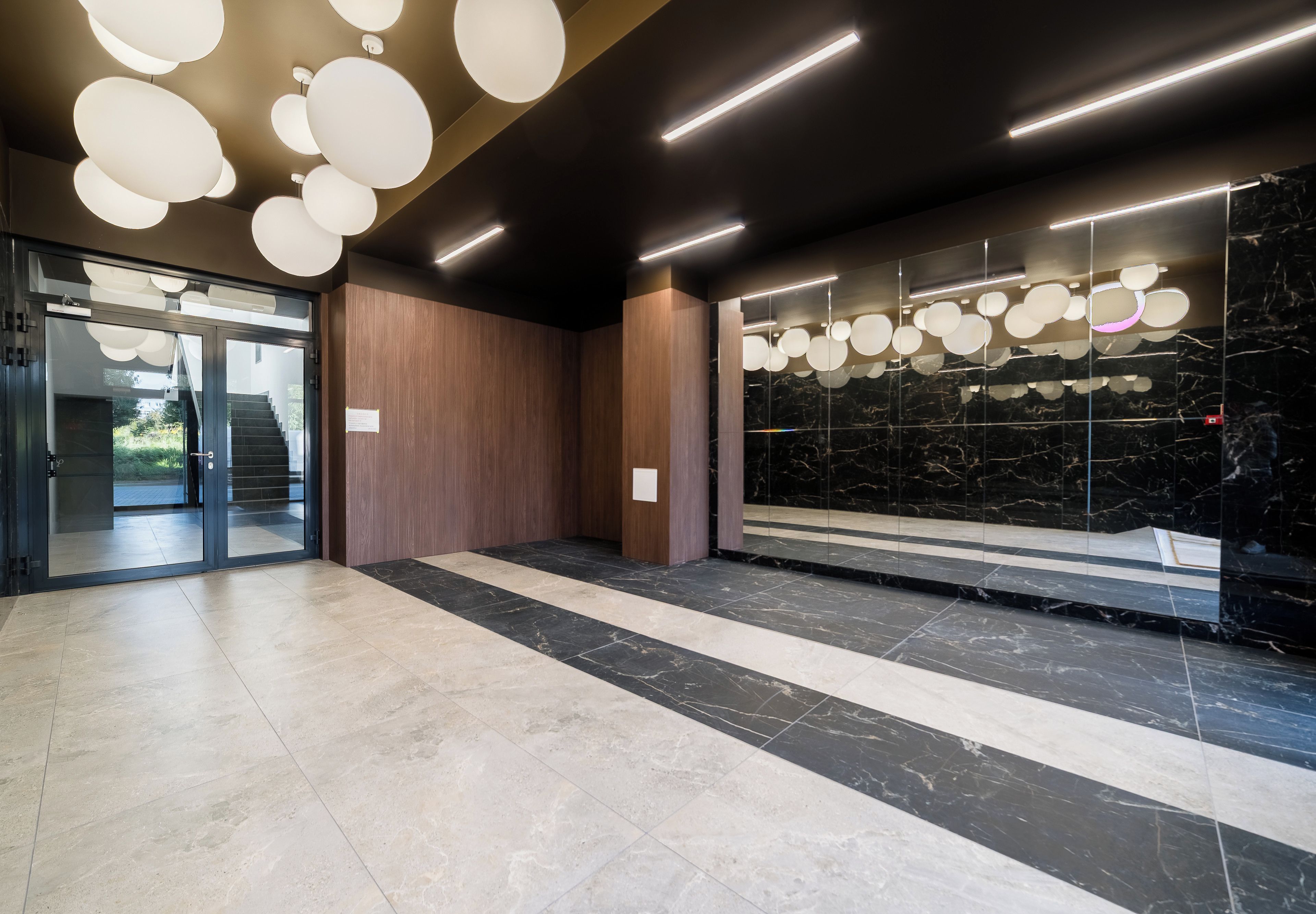 Un lobby moderno con piso de mármol, paneles de madera y entrada de vidrio.