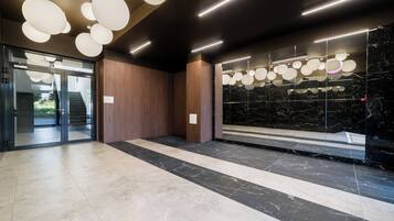 Un lobby moderno con piso de mármol, paneles de madera y entrada de vidrio.