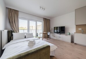 Quarto de hotel com cama, televisão, escrivaninha e vista para edifícios pela janela.