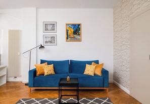Ein Zimmer mit einem blauen Sofa, zwei gelb gemusterten Kissen, einem schwarzen Couchtisch und drei gerahmten Bildern an der Wand.