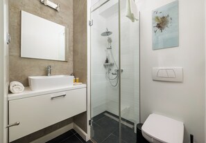 Un bagno moderno con cabina doccia in vetro, lavandino bianco e water.