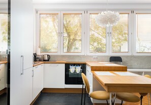 A modern kitchen with white cabinets, a wooden countertop, a black oven, and a dining area with a wooden table and chairs. - National Stadium Prime Location Studio (Warszawa)