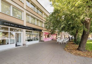 Ein Gebäude mit einer Schaufensterschild 'AGENCY NIERUCHOMOSCI' und einem Baumschattigen Bürgersteig.