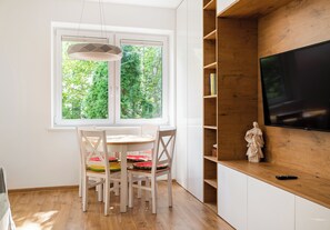 Eine moderne Küche mit Esstisch, Stühlen, einem Fenster mit Blick auf Grünflächen und einem an einer Holzwand montierten Fernseher.