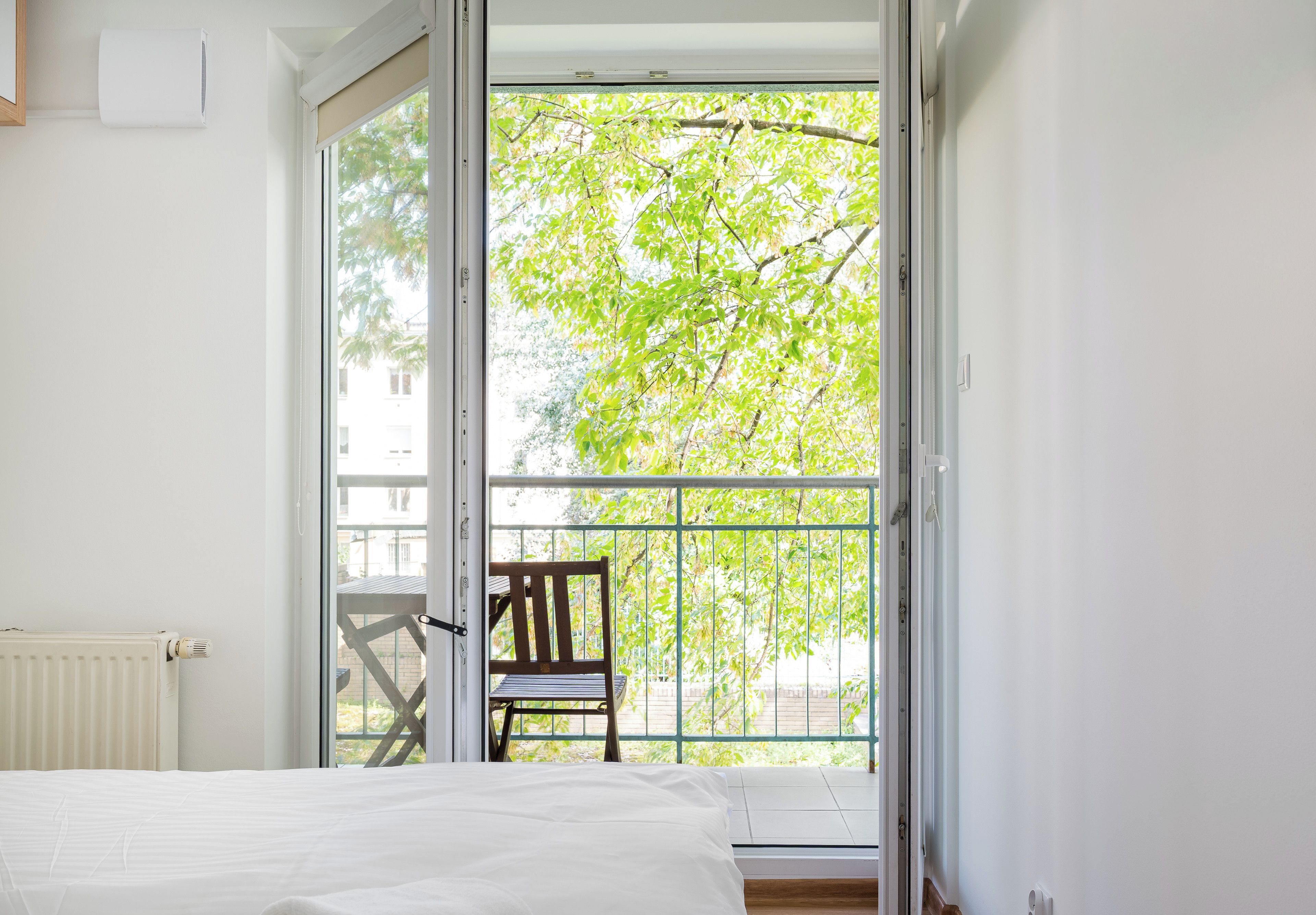 Un dormitorio con un amplio ventanal corredero que da a un balcón con una silla y vistas a árboles.