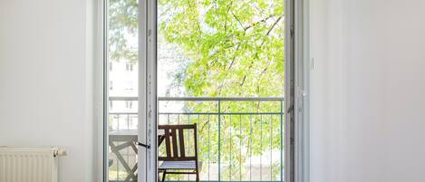 Un dormitorio con un amplio ventanal corredero que da a un balcón con una silla y vistas a árboles.
