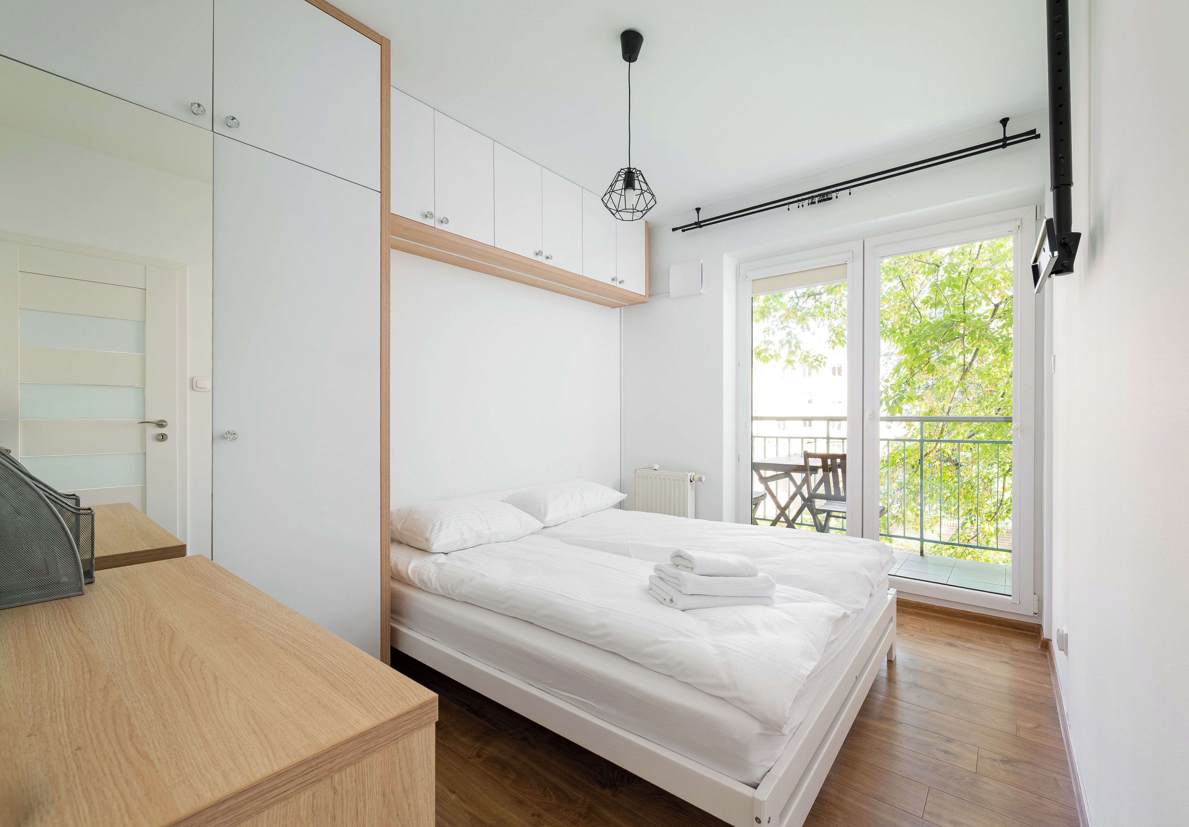 Un dormitorio con cama, escritorio de madera, radiador y vistas a la vegetación por la ventana.