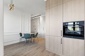 Eine moderne Küche mit hellen Holzschränken, einem schwarzen Backofen und einem Essbereich mit Türkis-Stühlen.