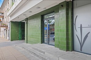Ein Gebäude mit einer grün gefliesten Fassade, einem Glastür-Eingang und einem Schild mit einem nach unten zeigenden Pfeil.