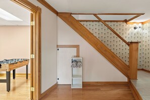 A room with a wooden staircase, a foosball table, and a white shelf unit. - Hot Tub | Sauna | Sleeps 6 (Canandaigua)