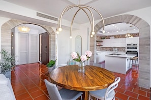 A modern kitchen with white cabinets, a central island, and a dining area with a wooden table and chairs. - Villa Gem Tropical Charm, Prime Location (Sabana)