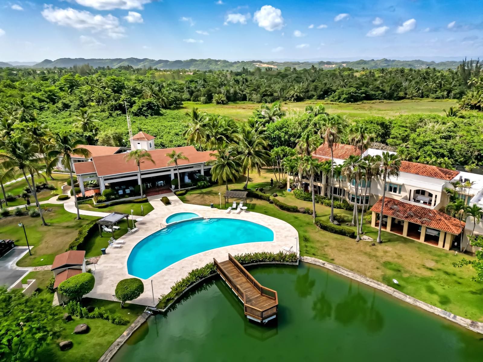 A resort with a large swimming pool, palm trees, and a view of distant hills.