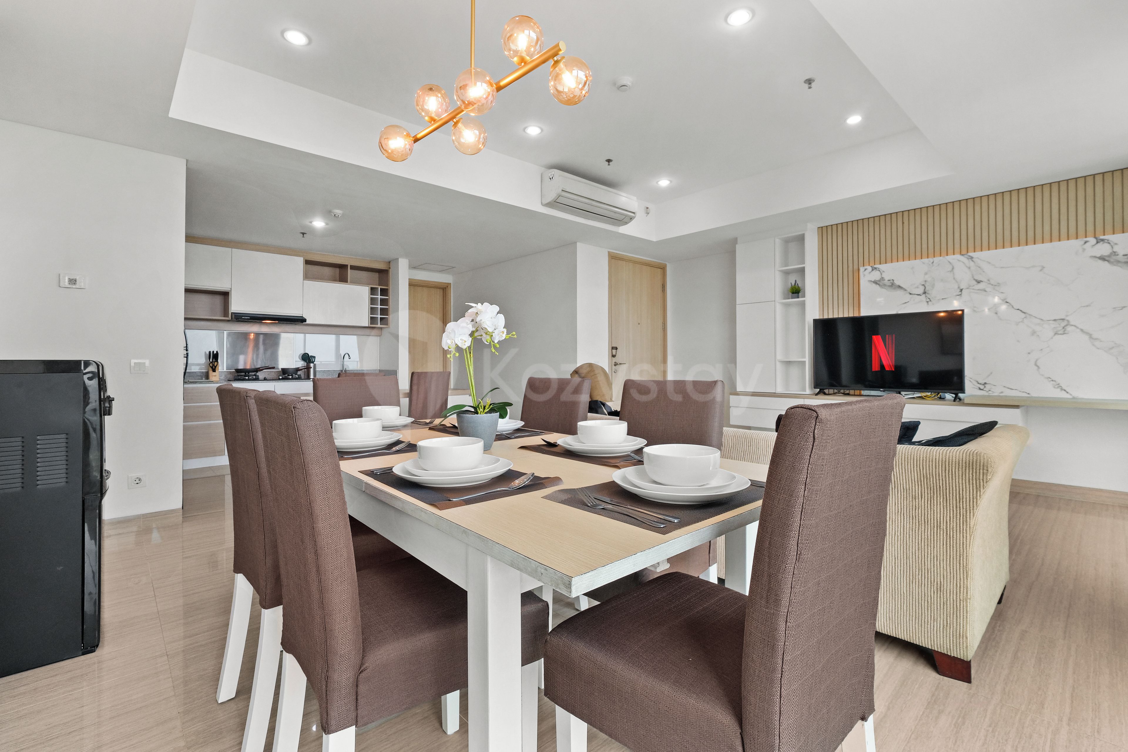 A modern dining area with a white table, brown chairs, and a chandelier.